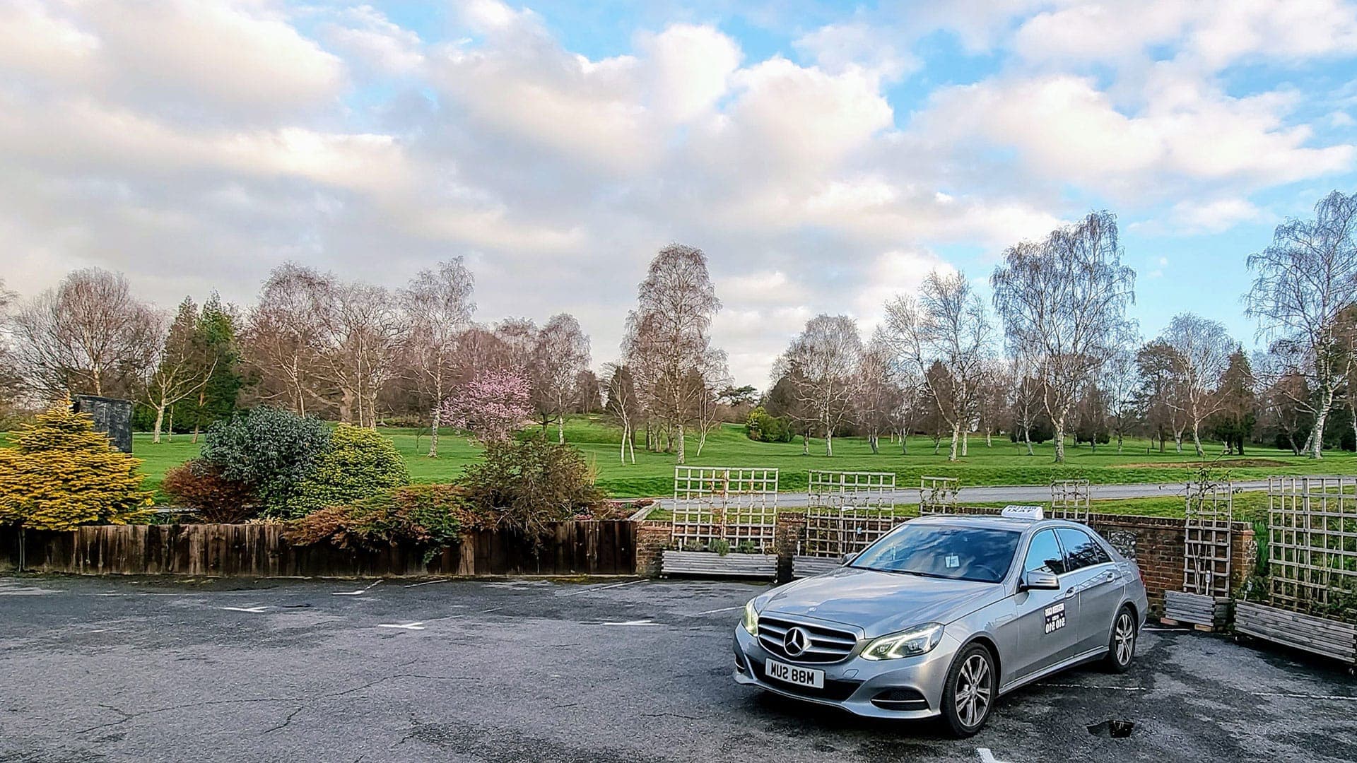 A silver Western Cars Mercedes saloon with a taxi roof sign, parked beside a golf course